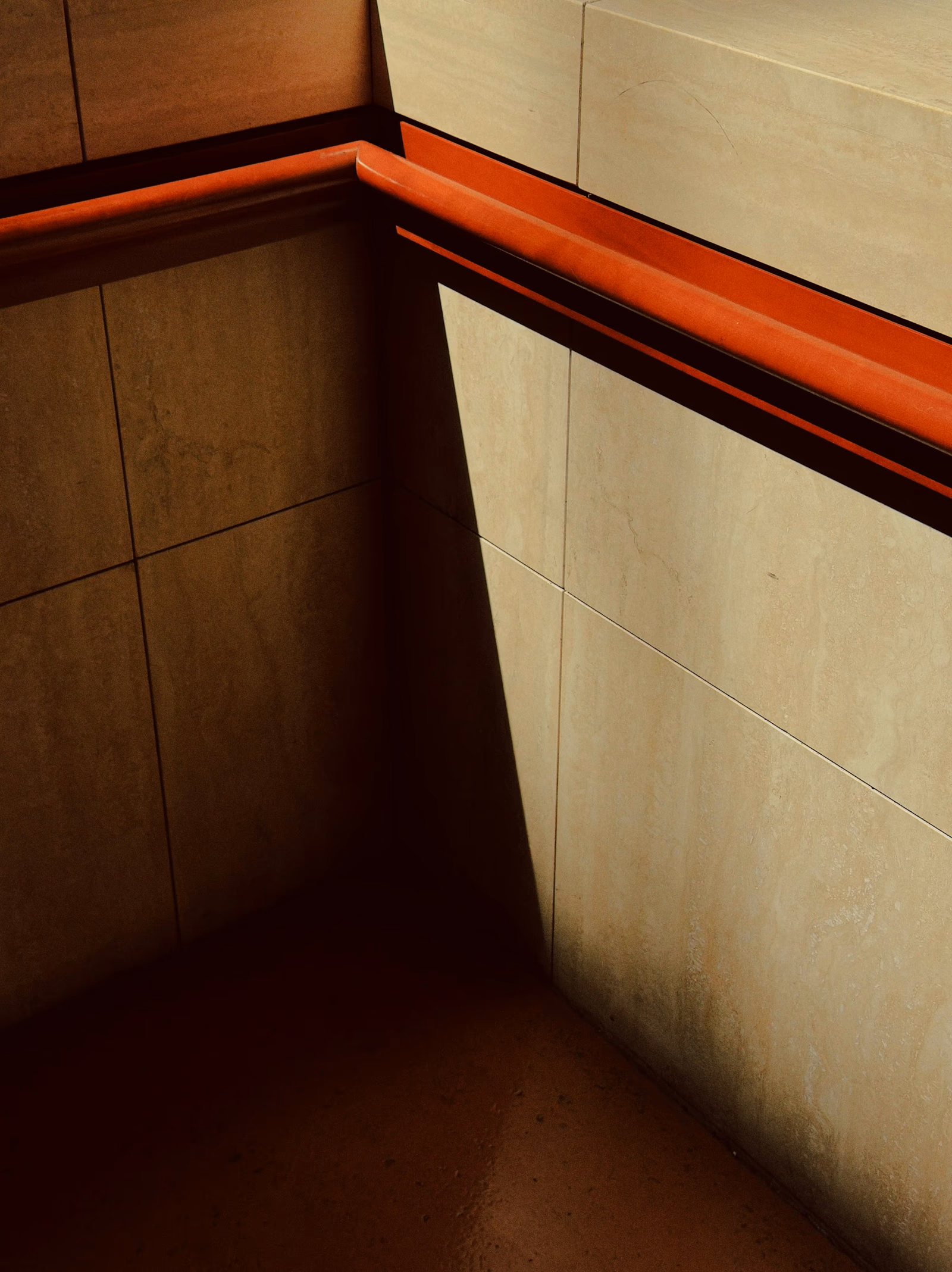 Corner of orange tiled walls with a sharp shadow along the trim