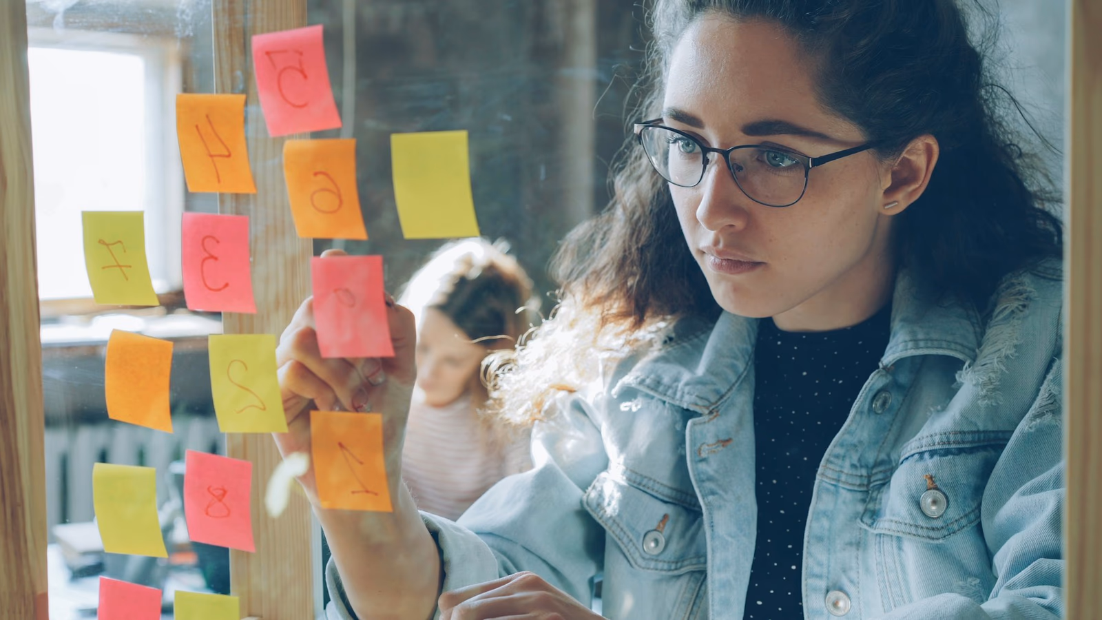Person reviewing colourful sticky notes arranged on glass